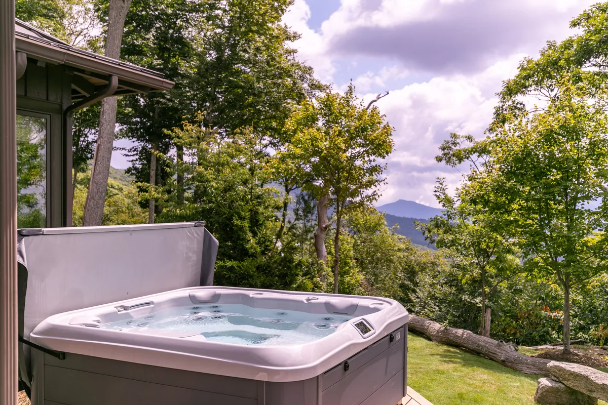 A luxurious outdoor hot tub sits nestled among trees with distant mountain views. The setup invites relaxation and socialization, offering a front-row seat to both sunrise and sunset, as well as opportunities for stargazing in the winter air.
