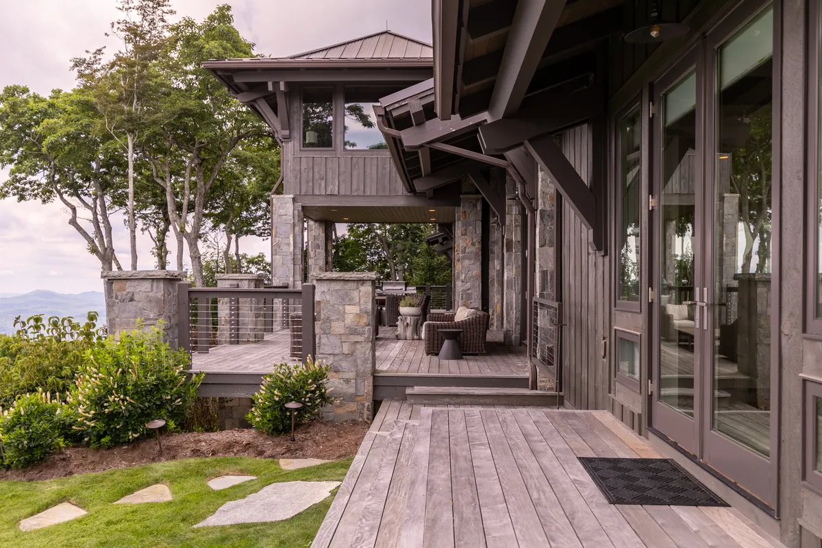 A tranquil wooden deck with a stone wall and outdoor seating, surrounded by lush greenery. The setting is perfect for relaxing, entertaining guests, or enjoying quiet moments in nature.
