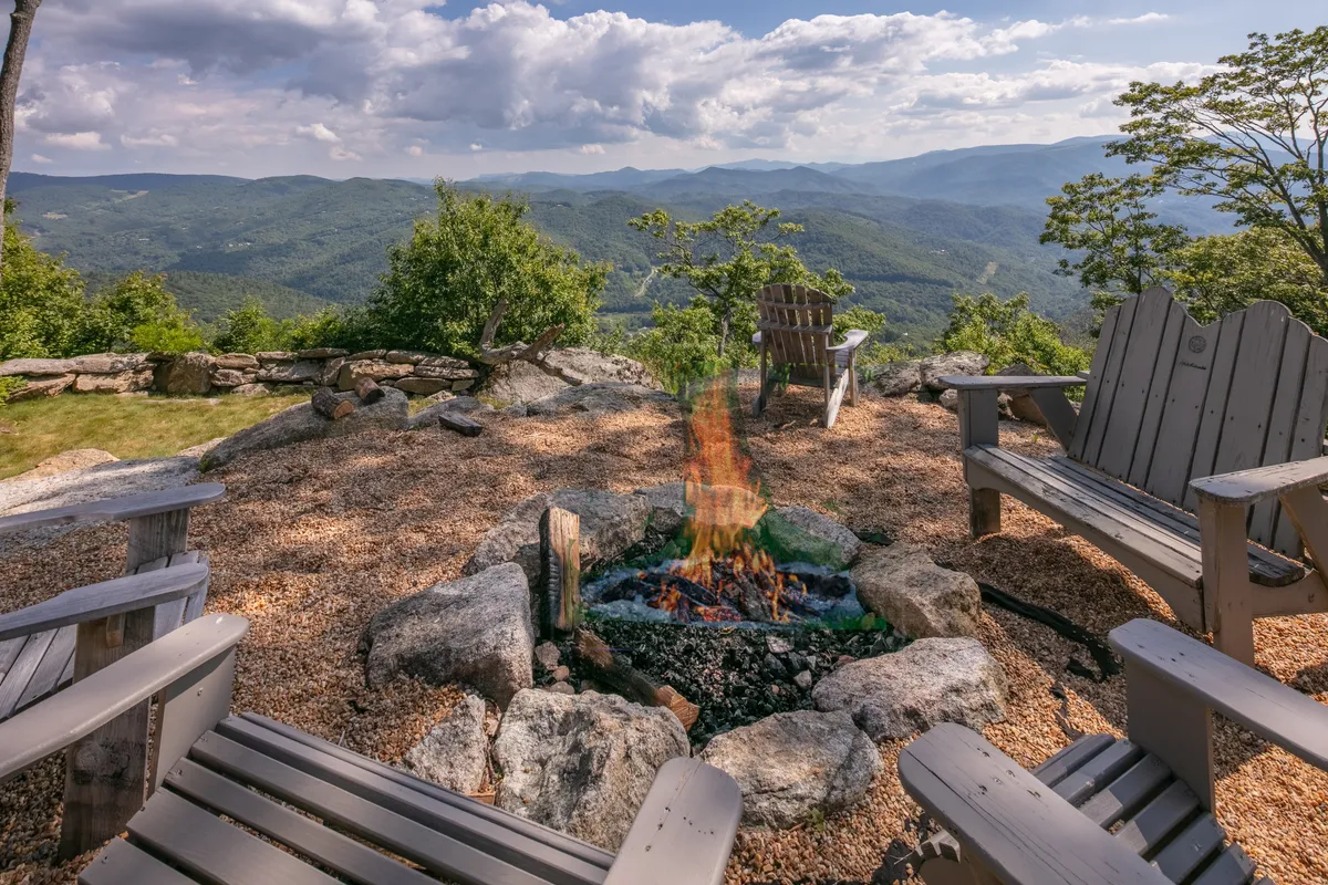 This exterior shot shows a fire pit surrounded by Adirondack chairs, set against a backdrop of surrounding mountains. The scene conveys relaxation and camaraderie as guests gather to share stories or stargaze after a day outdoors.
