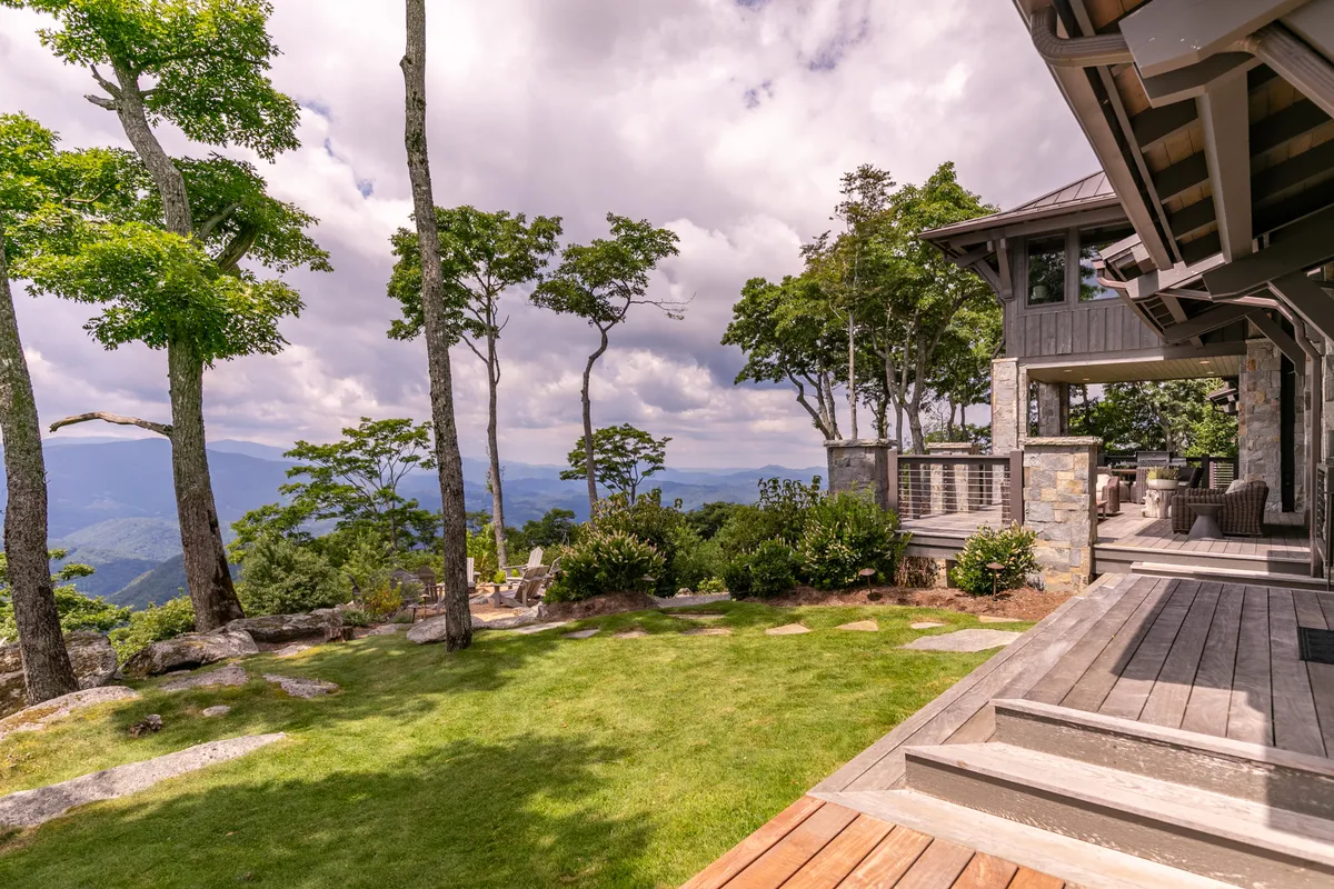 A serene exterior setting with a modern architectural home, a sweeping mountain view, and lush greenery. The scene suggests peaceful outdoor dining, relaxation, and the enjoyment of scenic vistas.