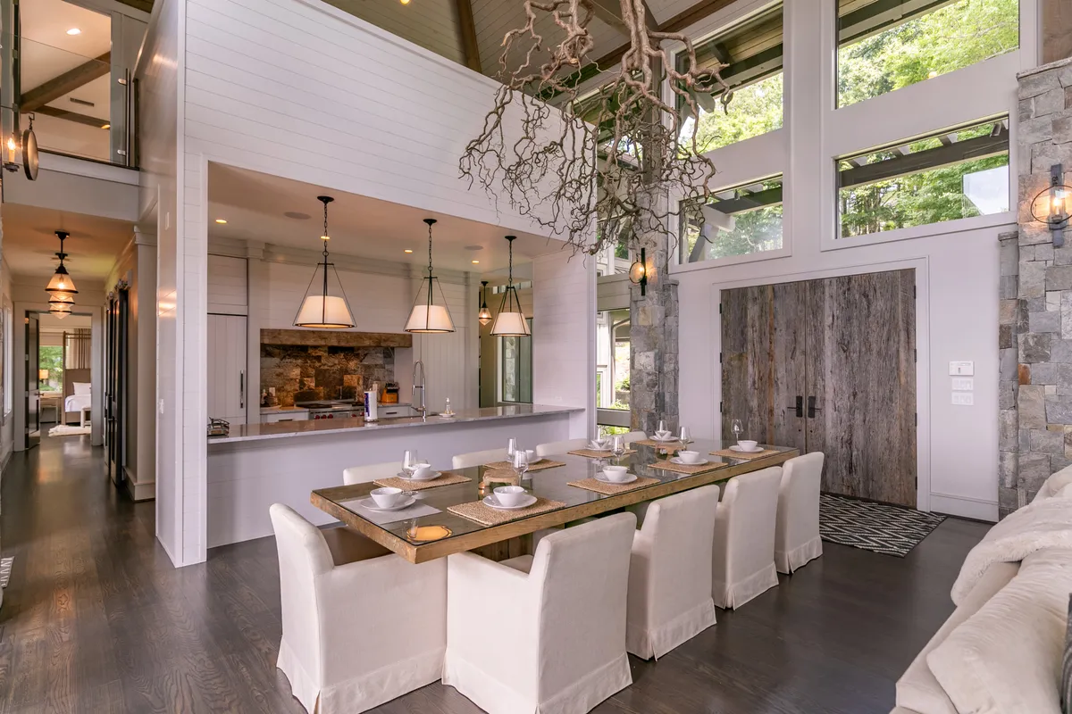 A spacious dining area featuring a large table, pendant light fixtures, and a stone accent wall. The open kitchen is visible in the background, reinforcing the seamless flow between dining and cooking spaces. The mood is warm, inviting, and ideal for both festive meals and quiet brunches.