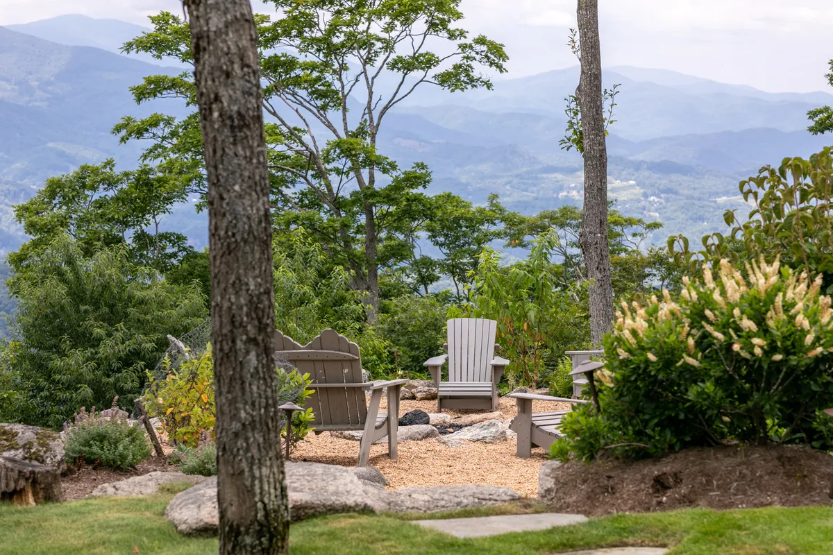 An exterior seating arrangement with Adirondack chairs surrounding a fire pit, set against a panoramic mountain view and lush greenery. The setup is ideal for stargazing, sharing stories, or unwinding after a day of adventure.