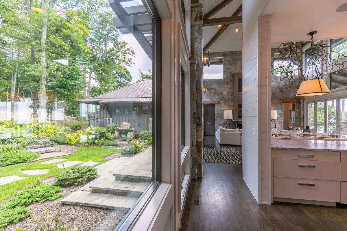 A kitchen island serves as a focal point, framed by stone walls and large windows that open onto an outdoor garden. The space is flooded with natural light and designed for gatherings, with plenty of room for cooking, entertaining, and enjoying sunrise coffee with a view.