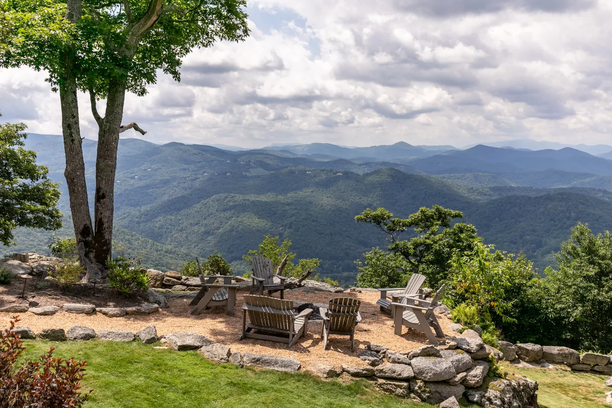 A tranquil view scene showing comfortable seating set against a sweeping mountain backdrop, framed by trees. The space is ideal for unwinding, socializing, or simply admiring the changing landscape, whether in the glow of sunset or under a starlit sky.